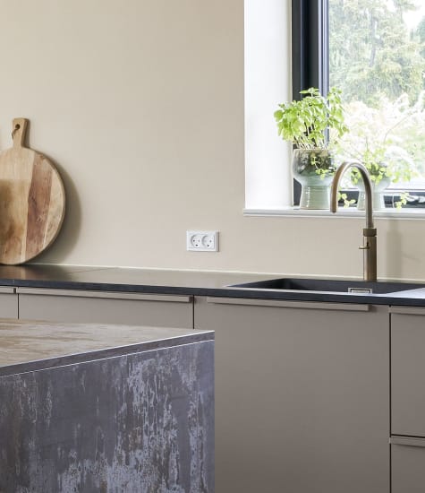 Moderne køkken med beige skabe, sort bordplade og trædetaljer | HTH
