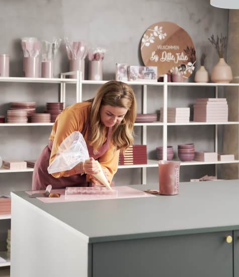 Person decorating cake on green kitchen island with shelves in background | HTH