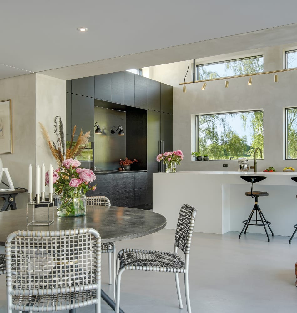 Open kitchen with white kitchen island and black cabinets, featuring woven chairs | HTH