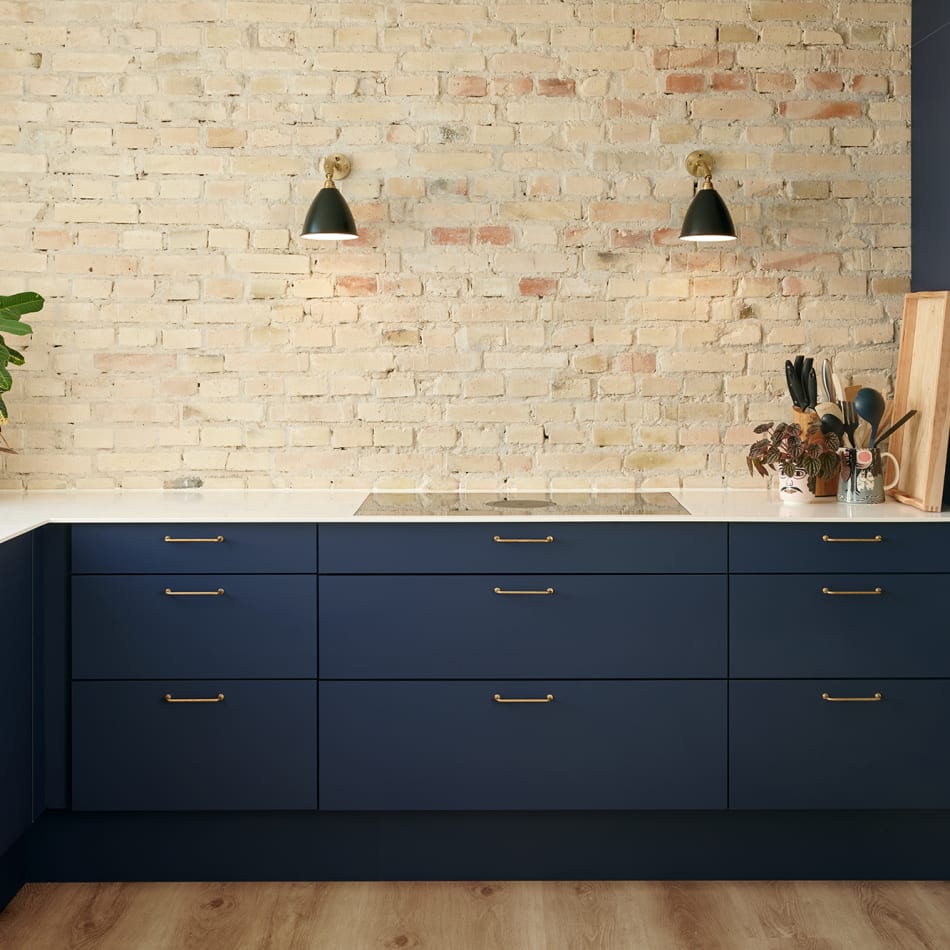 Navy blue kitchen cabinets with white countertop and brick wall backdrop | HTH