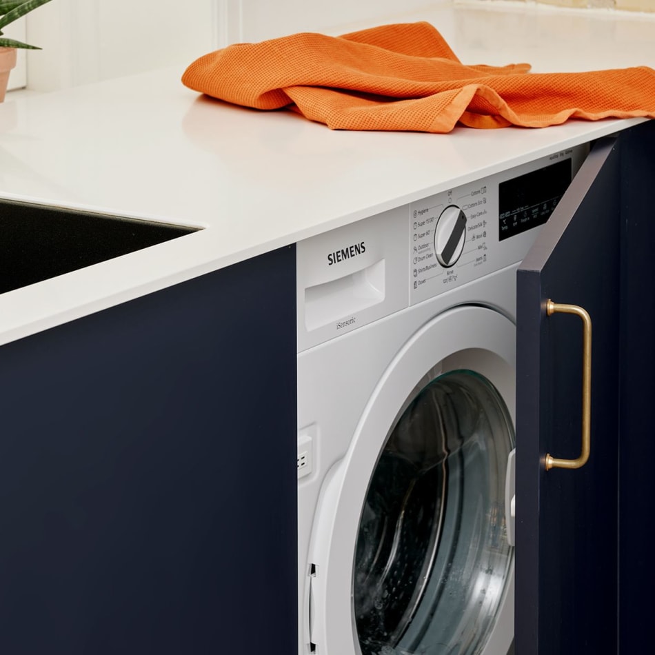 Navy kitchen cabinet with white countertop and built-in washing machine | HTH