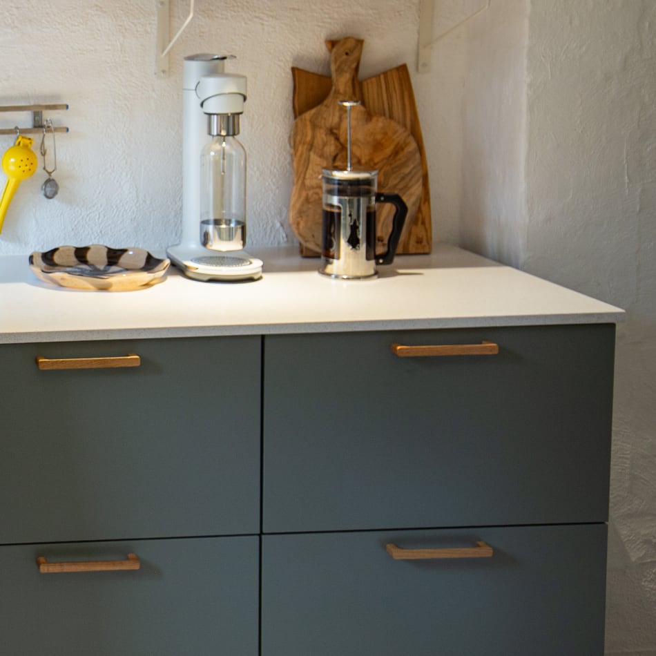 Green cabinetry with white countertops and wooden hardware | HTH