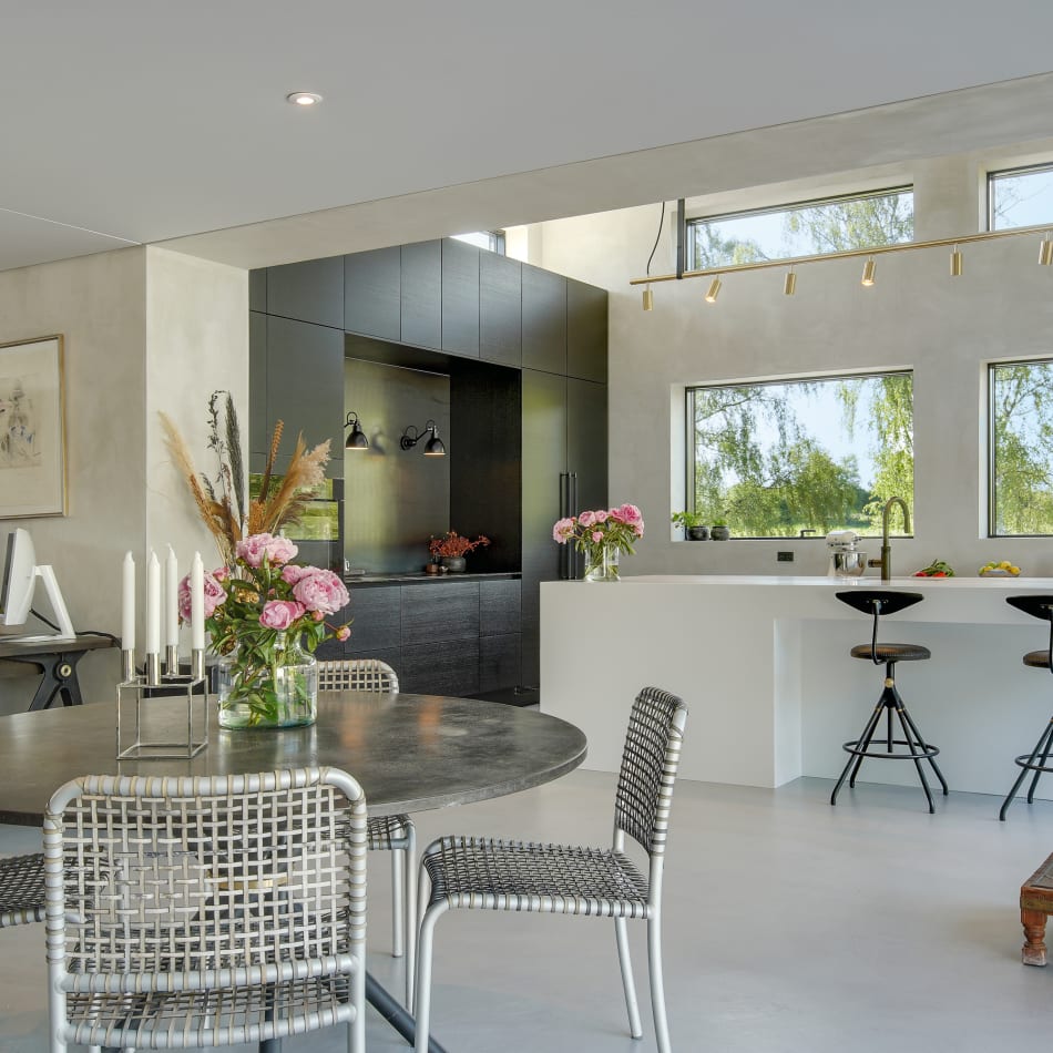 Open kitchen with white kitchen island and black cabinets, featuring woven chairs | HTH
