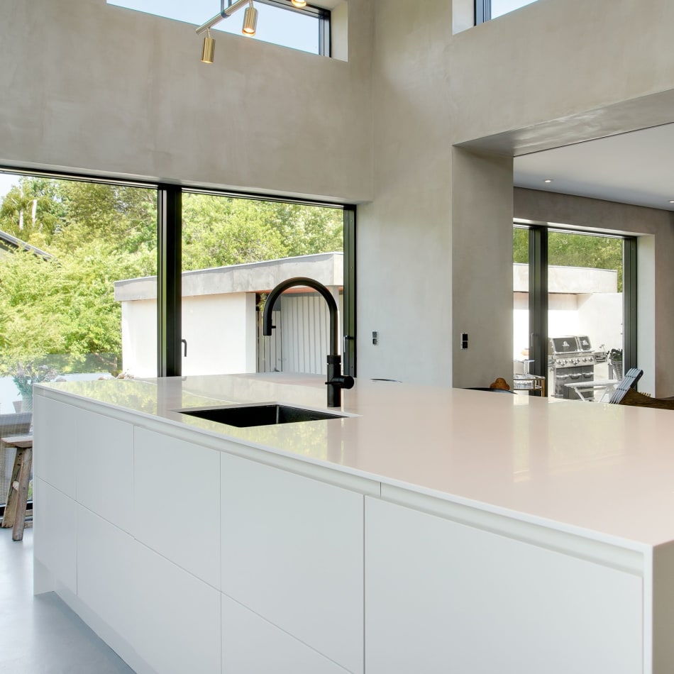 White kitchen island with black faucet and large windows in background | HTH