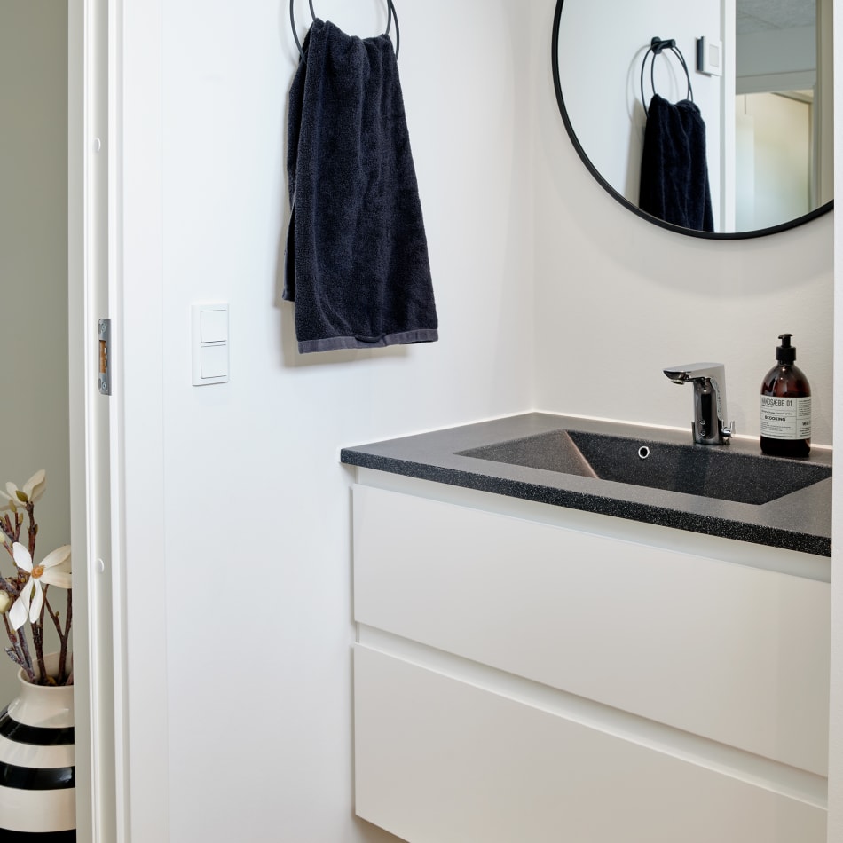 White bathroom vanity with black countertop and round mirror | HTH