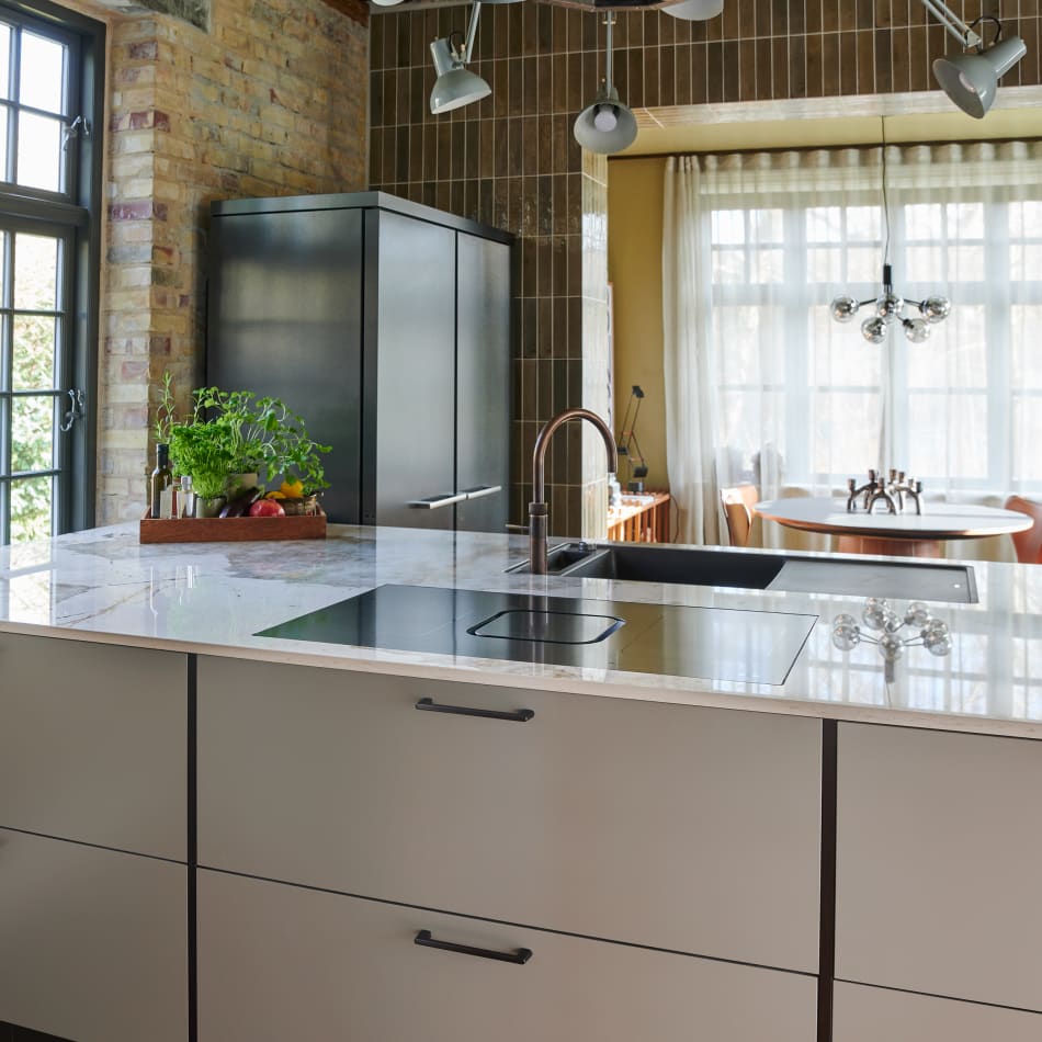 White kitchen island with black handles and integrated cooktop in a brick-walled kitchen | HTH