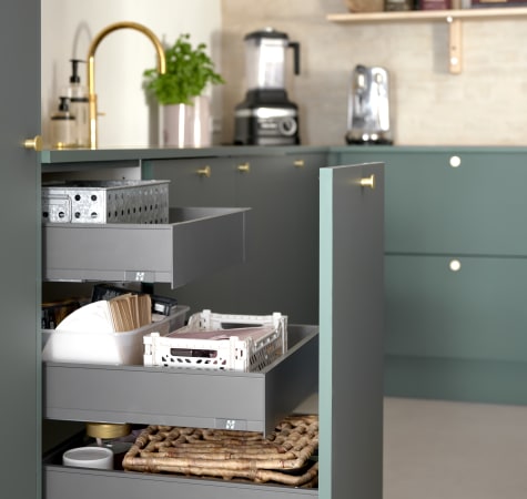 Green kitchen cabinets with open drawers, gold handles, and visible kitchenware | HTH
