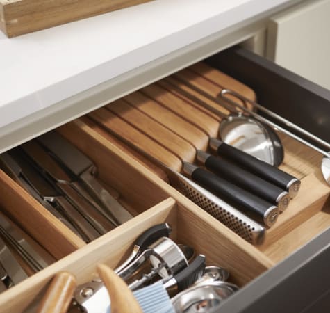 Open kitchen drawer with wooden dividers and utensils. White countertop visible | HTH