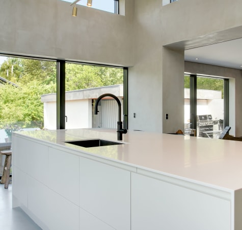 White kitchen island with black faucet and large windows in background | HTH