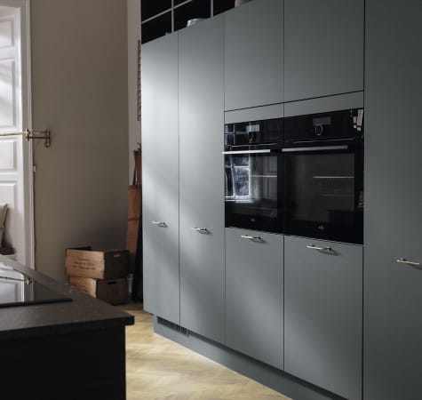 Green kitchen cabinets with built-in oven and dark countertop. Model Base | HTH