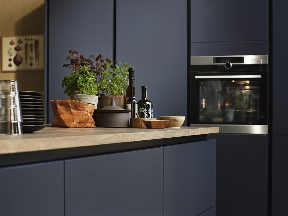 Midnight blue kitchen cabinets with light wood countertop and built-in oven. Focus | HTH