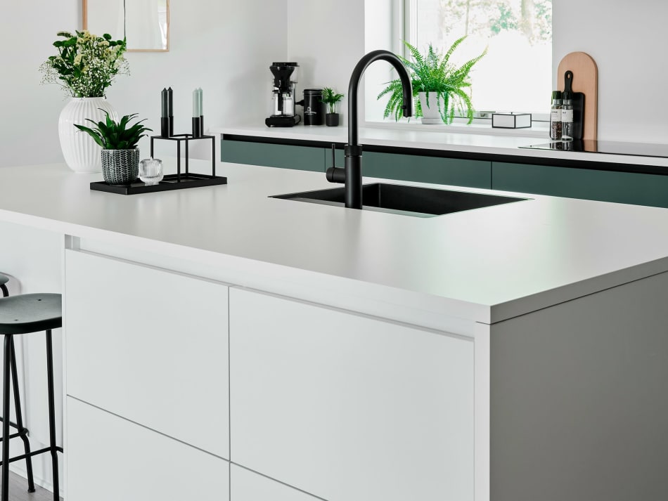 White kitchen island with integrated sink and dark faucet, green cabinets in background | HTH
