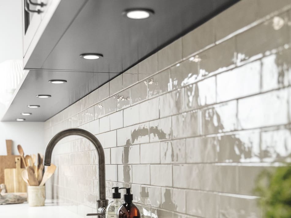 Gray tile backsplash with under-cabinet lighting and dark faucet. Model Art | HTH