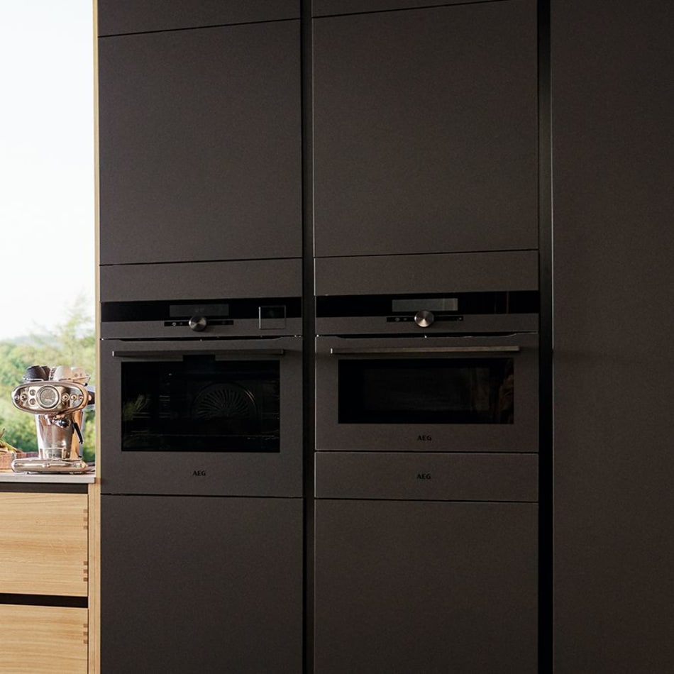 Black kitchen cabinets with built-in ovens and light wood panel on the side. Nordic Creation | HTH